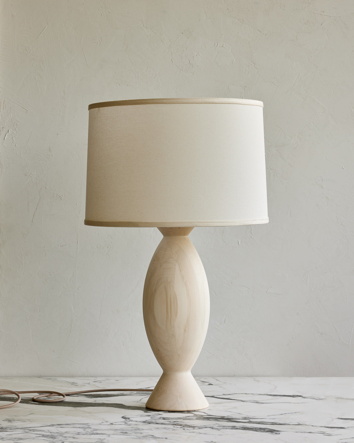 A traditional style table lamp with a round beige shade and a wooden base, possibly made of walnut or aspen wood. #wood-finish_aspen
#shade-color_ivory linen