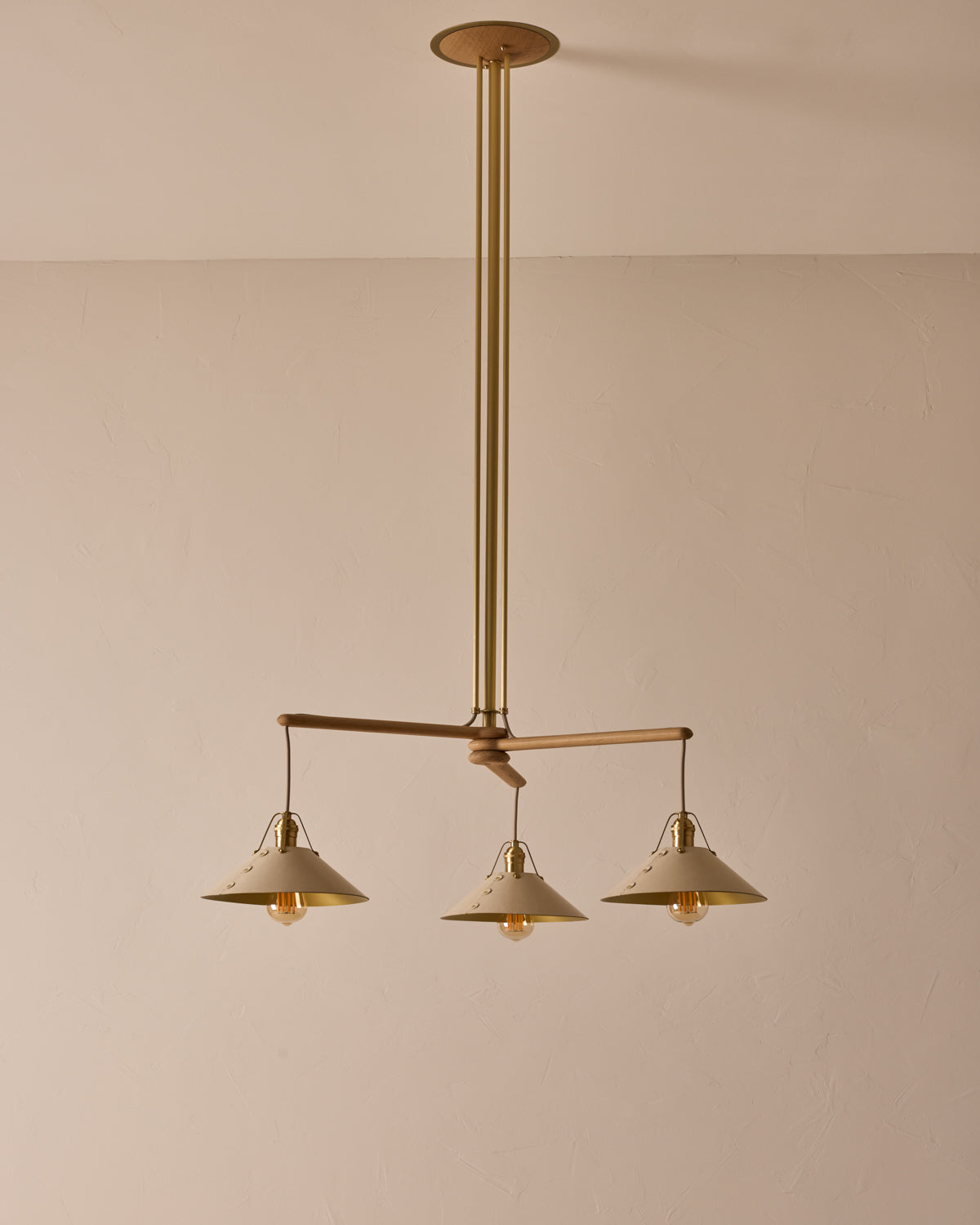 A three-arm chandelier with brass metal poles and white leather shades, suspended from a white oak canopy. #leather-shade_eggshell