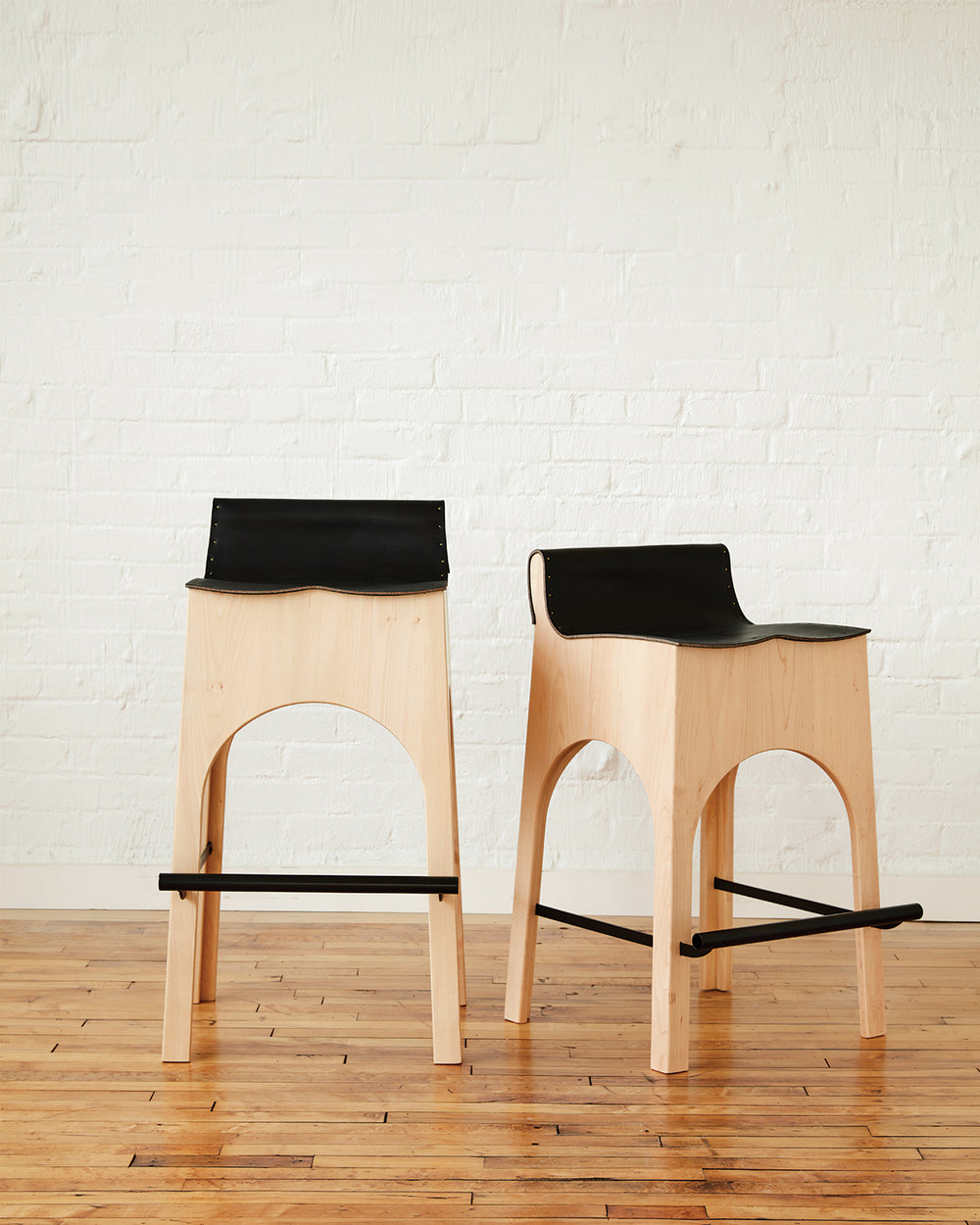 Sculpted stool with black leather and maple wooden base with metal foot rest and short backrest. Counter and bar height. Handmade in Philadelphia by Lostine. Simple Interior Design. Warm American Modern Design #leather-finish_black harness