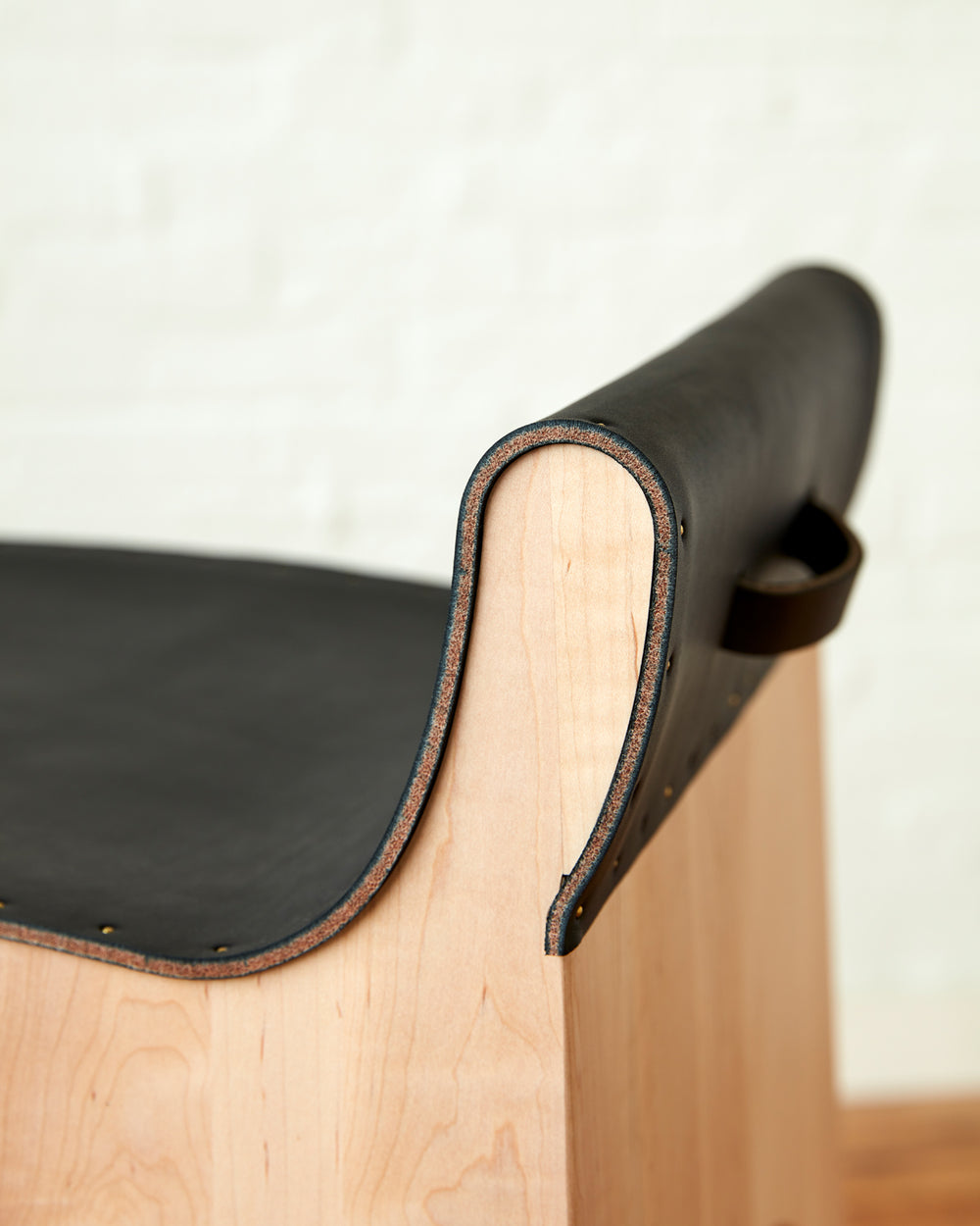 Sculpted stool with black leather and maple wooden base with metal foot rest and short backrest. Counter and bar height. Handmade in Philadelphia by Lostine. Simple Interior Design. Warm American Modern Design #leather-finish_black harness