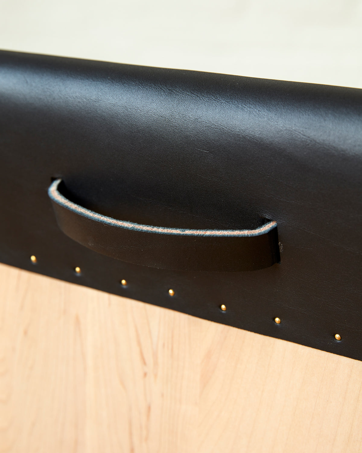 Leather pull handle of Sculpted stool with black leather and maple wooden base with metal foot rest and short backrest. Counter and bar height. Handmade in Philadelphia by Lostine. Simple Interior Design. Warm American Modern Design #leather-finish_black harness