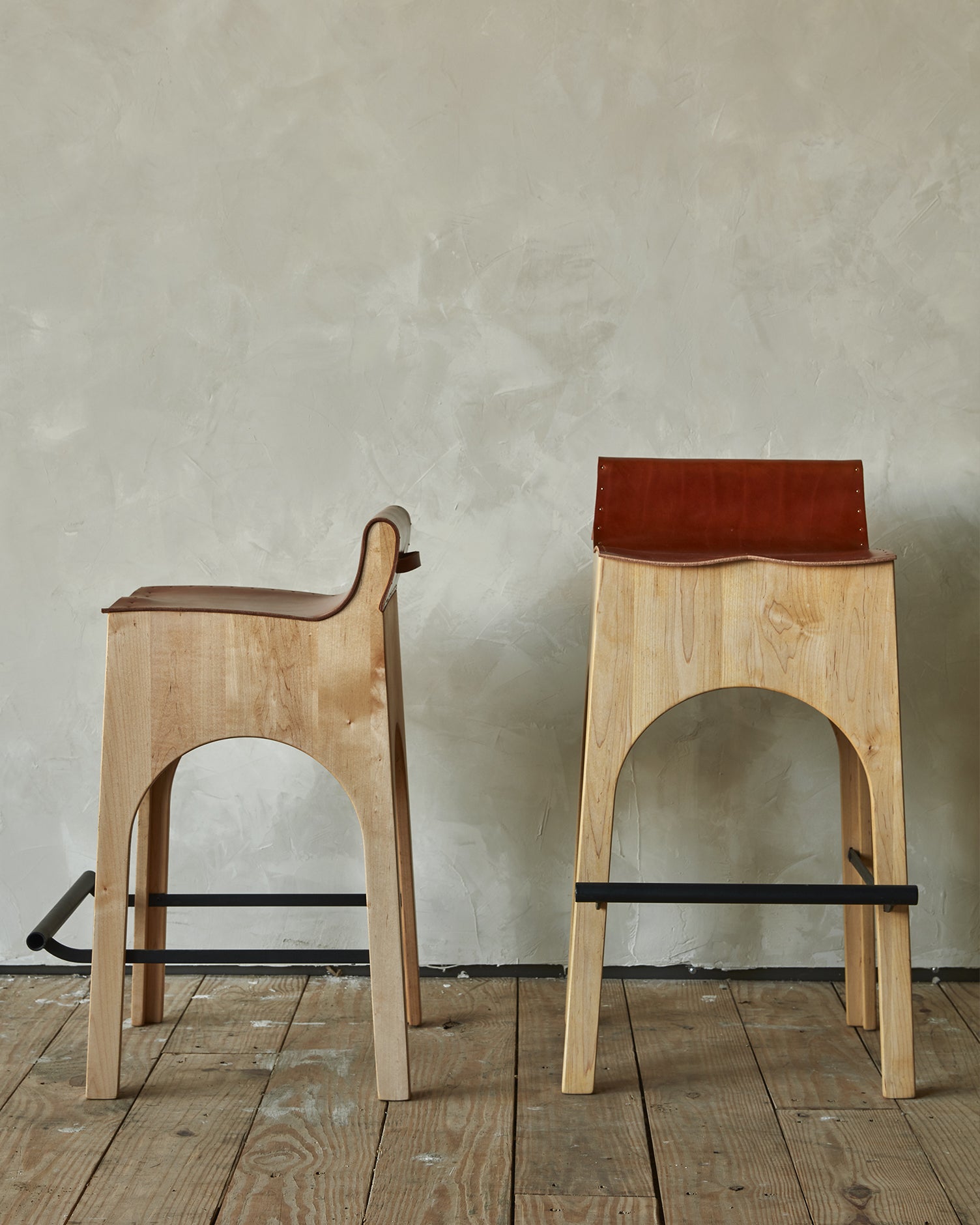 Sculpted stool with tan leather and maple wooden base with metal foot rest and short backrest. Counter and bar height. Handmade in Philadelphia by Lostine. Simple Interior Design. Warm American Modern Design #leather-finish_tan harness