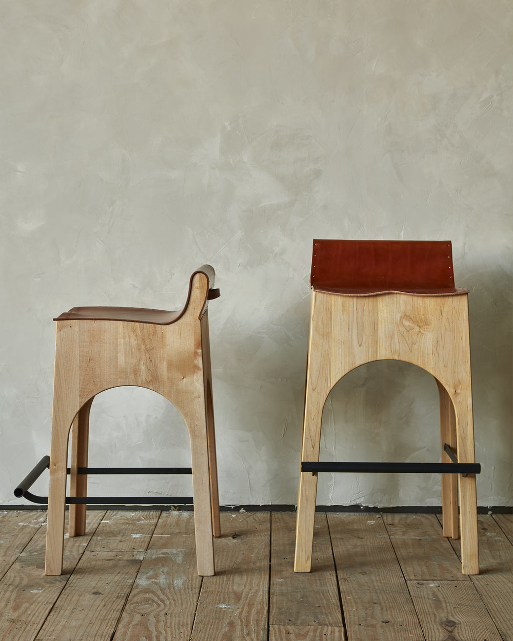Sculpted stool with tan leather and maple wooden base with metal foot rest and short backrest. Counter and bar height. Handmade in Philadelphia by Lostine. Simple Interior Design. Warm American Modern Design #leather-finish_tan harness